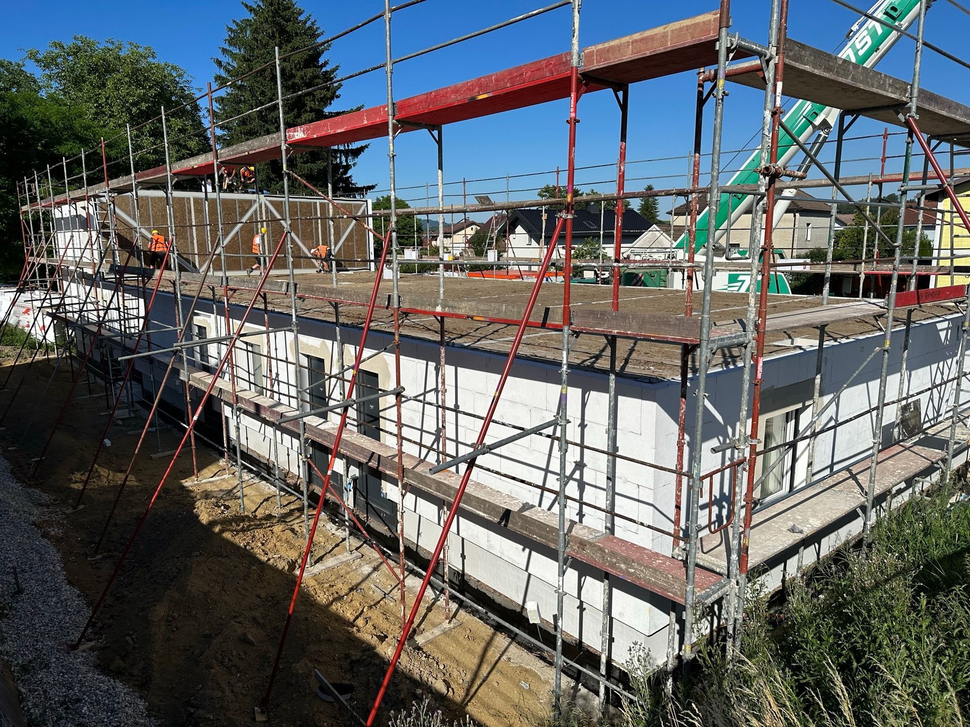 Baustelle mit Gerüst um ein einstöckiges Gebäude; blauer Himmel, grünes Gras.