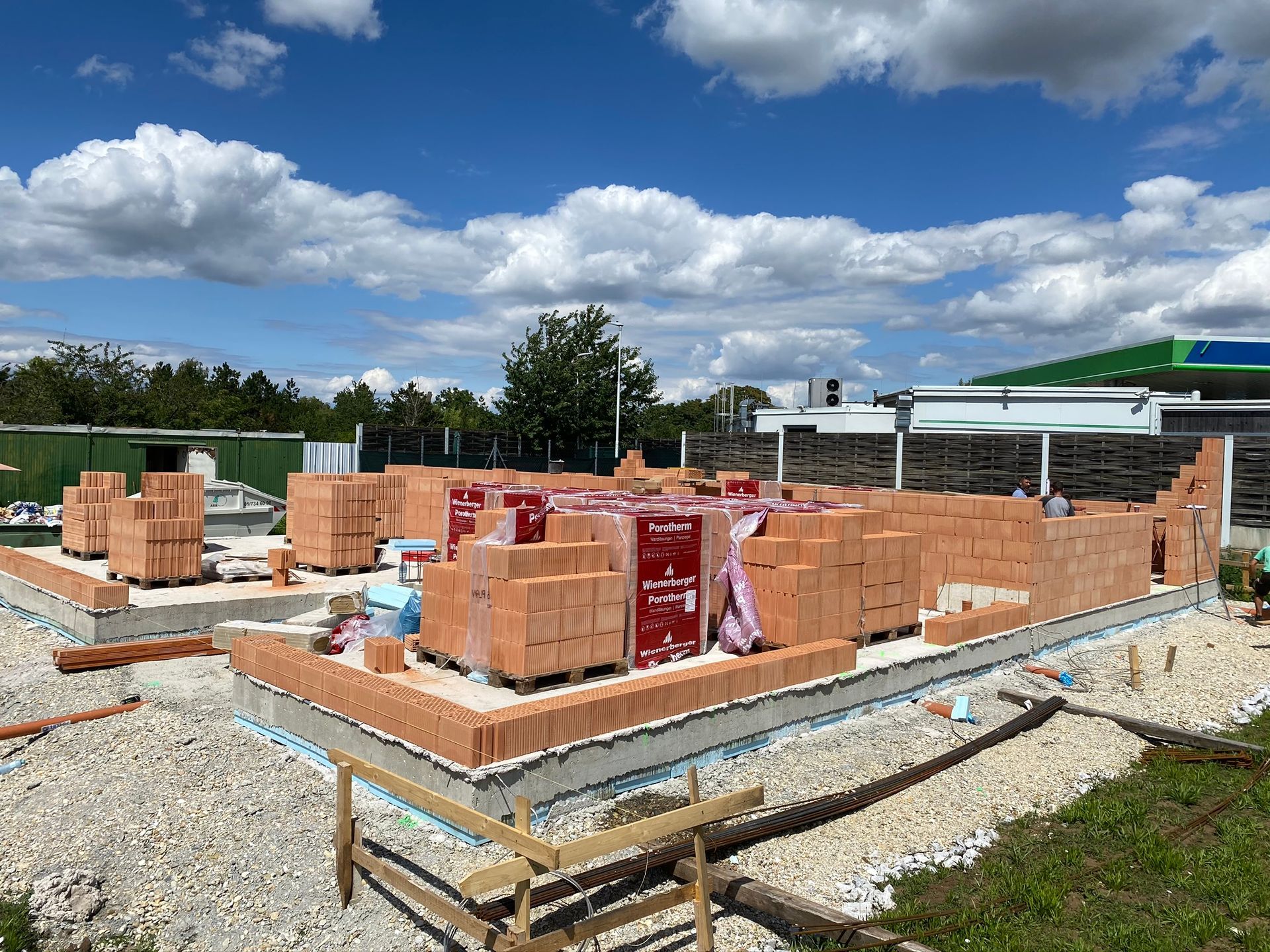 Ziegelbaustelle auf einem Schotteruntergrund mit Ziegelstapeln, blauem Himmel und Wolken darüber.