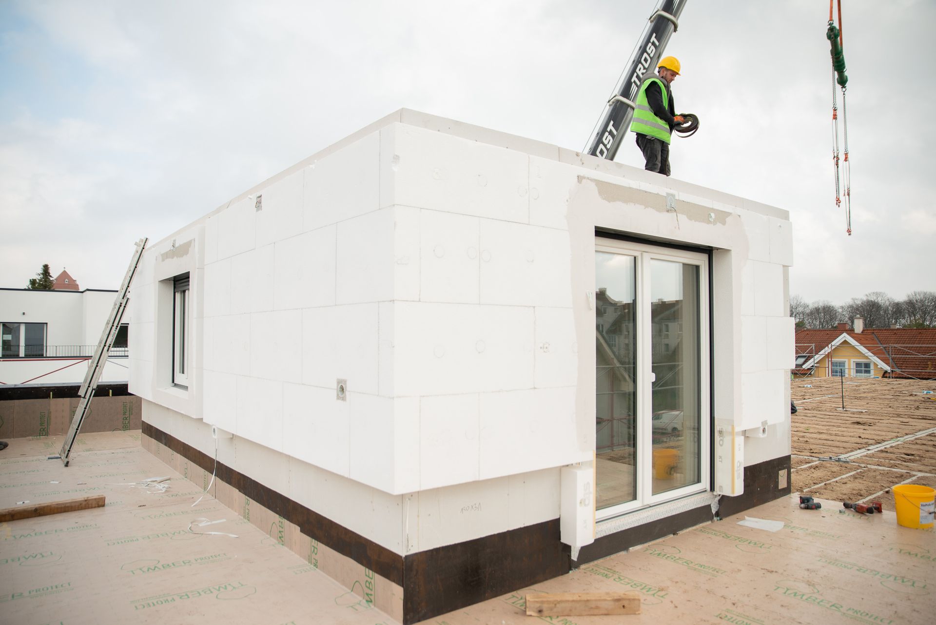 Bauarbeiter auf einem Dach, der mit einem Kran ein weißes modulares Gebäude aufstellt.