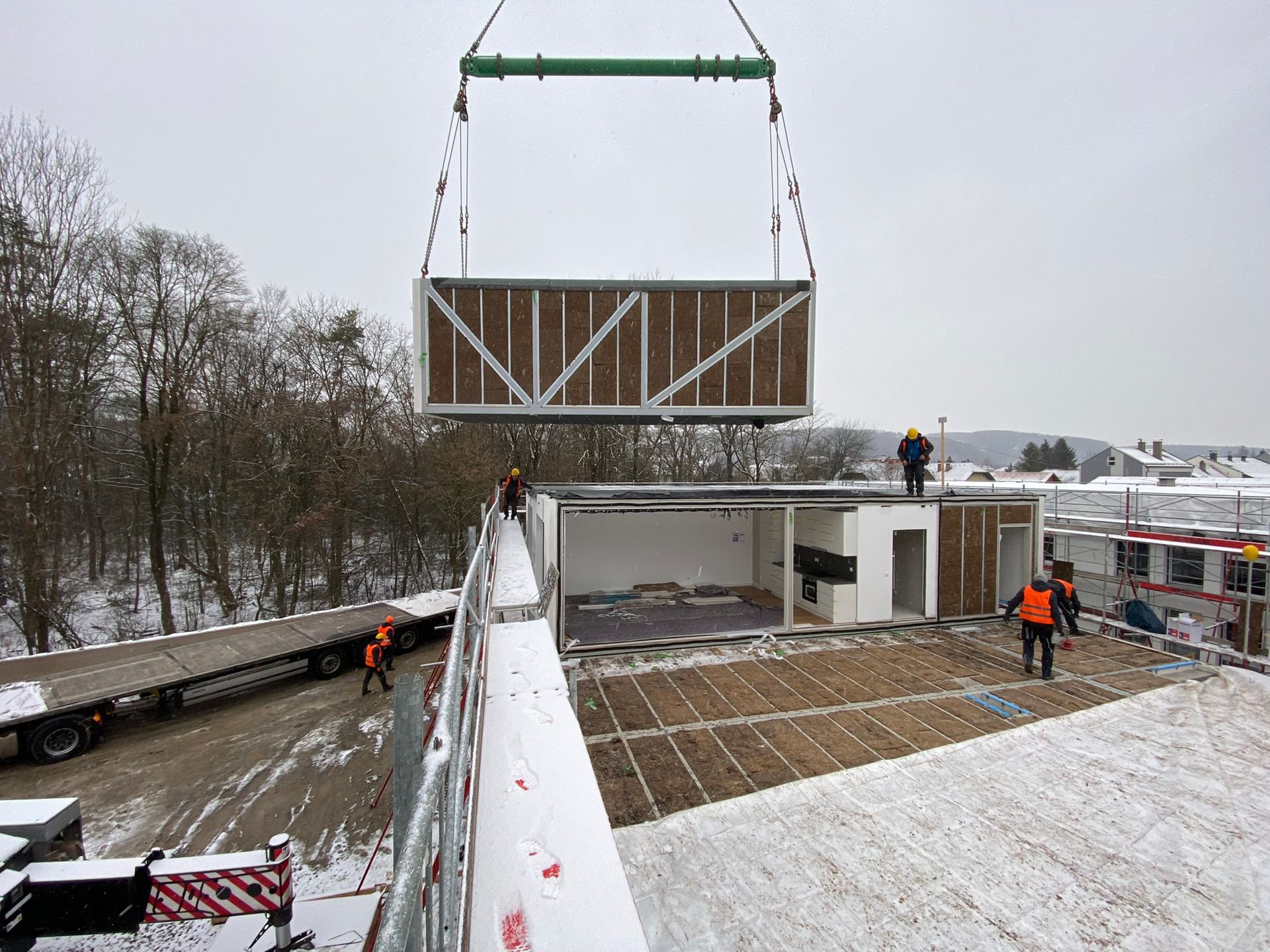 Ein modulares Gebäudeelement wird mit einem Kran angehoben und auf einer teilweise errichteten Struktur platziert 