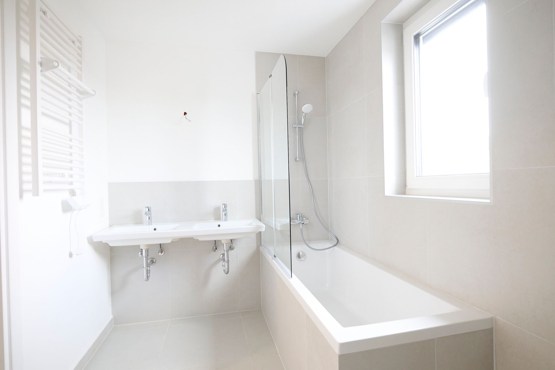 Strahlend weißes Badezimmer mit Doppelwaschbecken, Badewanne und Fenster.