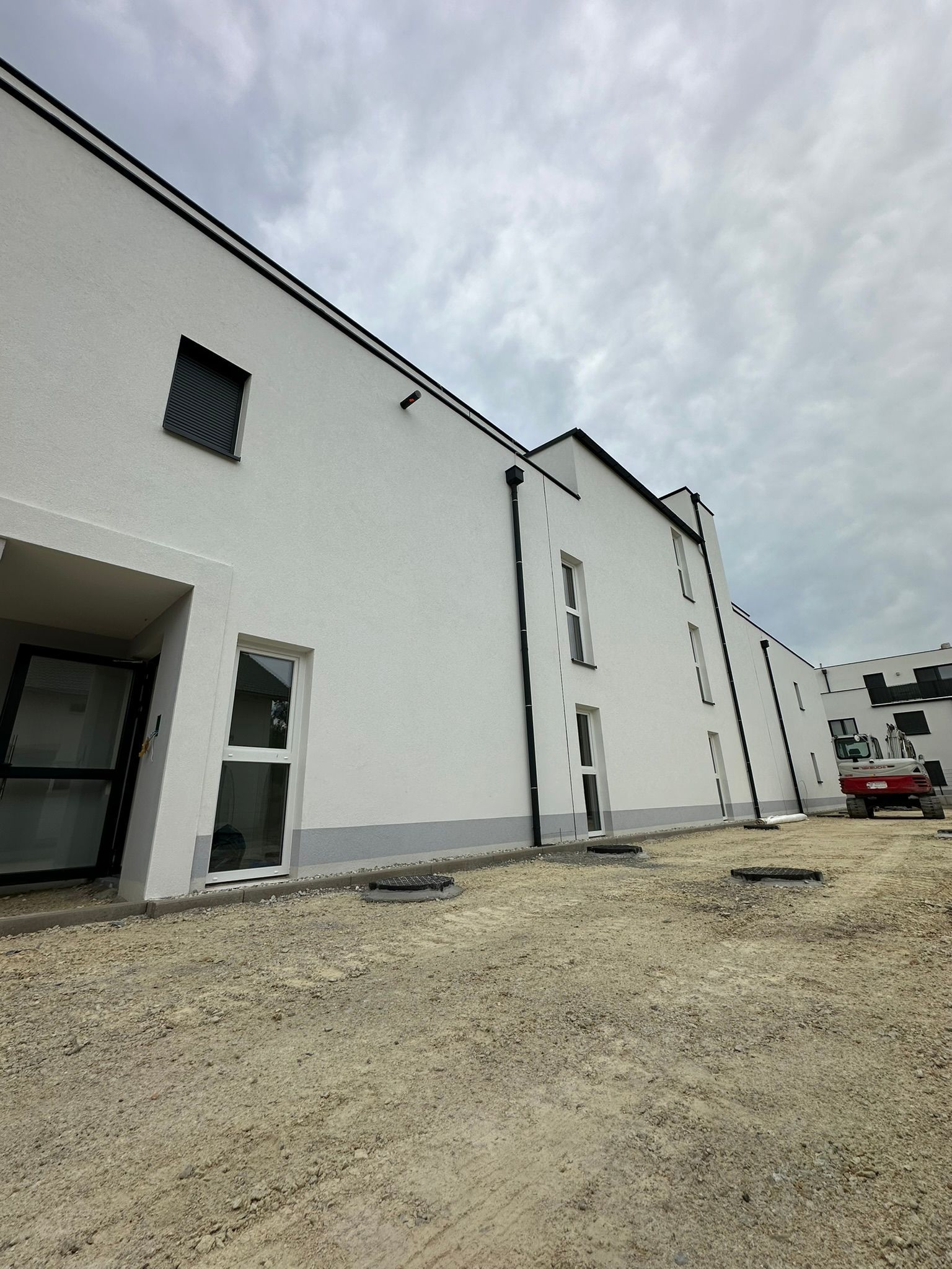 Weiße Gebäude mit schwarzen Verzierungen auf einem Schotterplatz unter einem bewölkten Himmel.