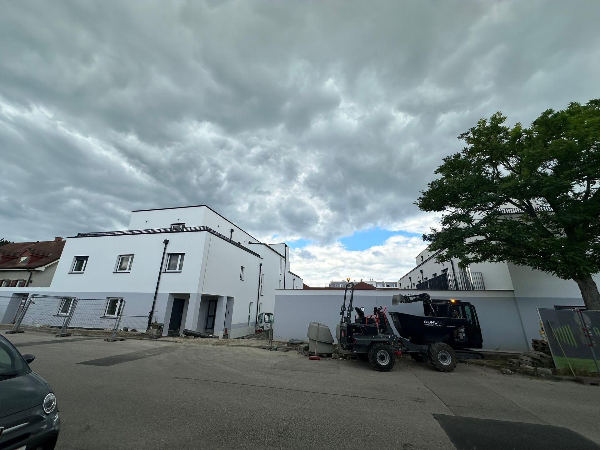 Baustelle mit weißen Gebäuden, einem kleinen Traktor und bewölktem Himmel.