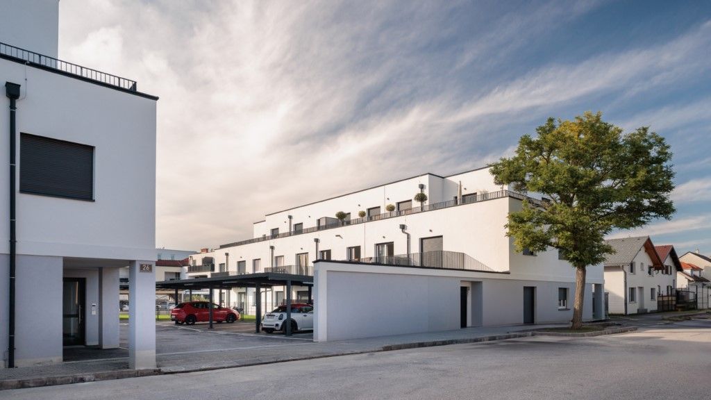 Weiße, moderne Stadthäuser mit unter einem Carport geparkten Autos, blauer Himmel.