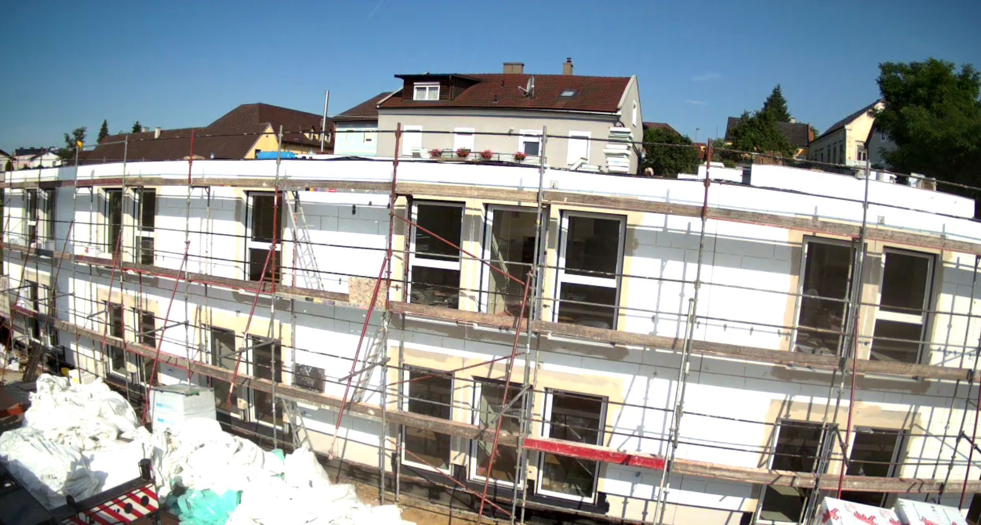 Baustelle; mehrstöckiges Gebäude im Umbau mit Gerüst, Styropor-Isolierung und blauem Himmel.