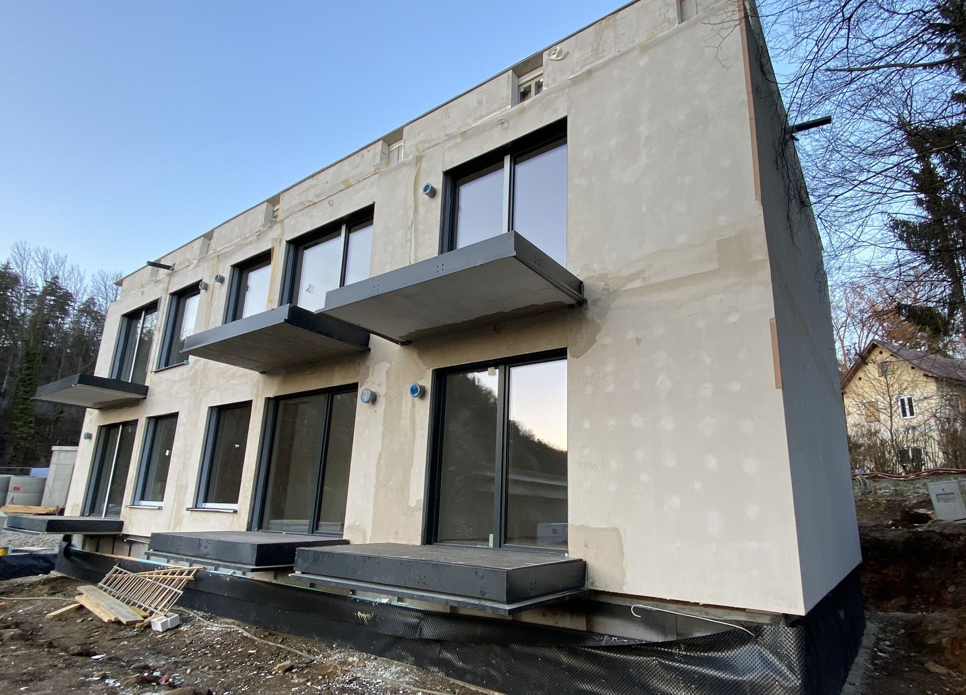 Mehrstöckige, moderne Stadthäuser im Bau, mit Balkonen und großen Fenstern; blauer Himmel.