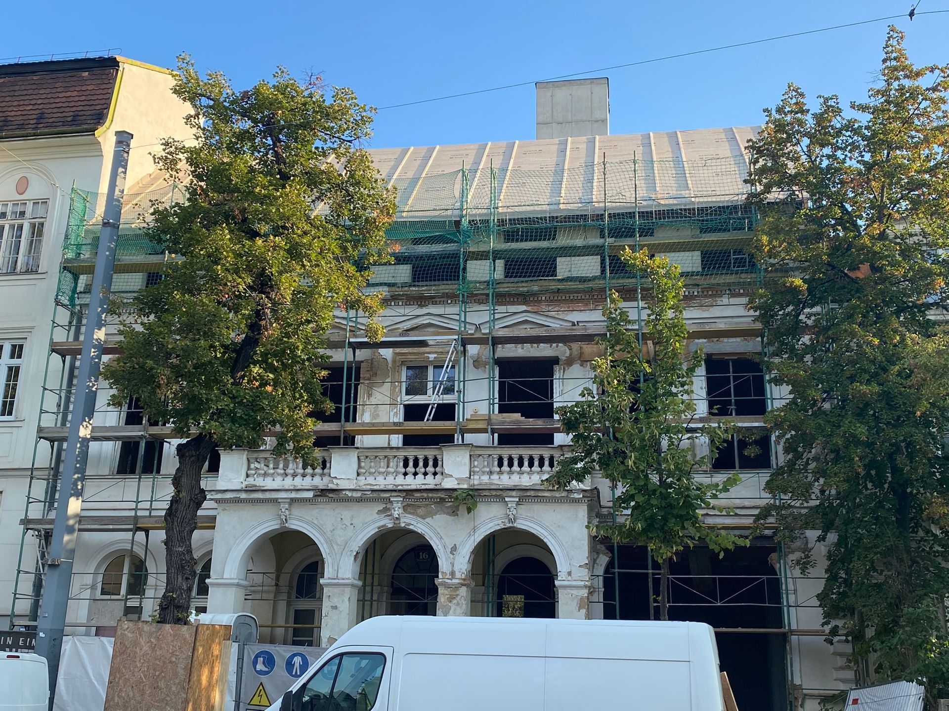 Gebäudefassade im Umbau; Gerüst, gewölbter Eingang, Bäume davor.