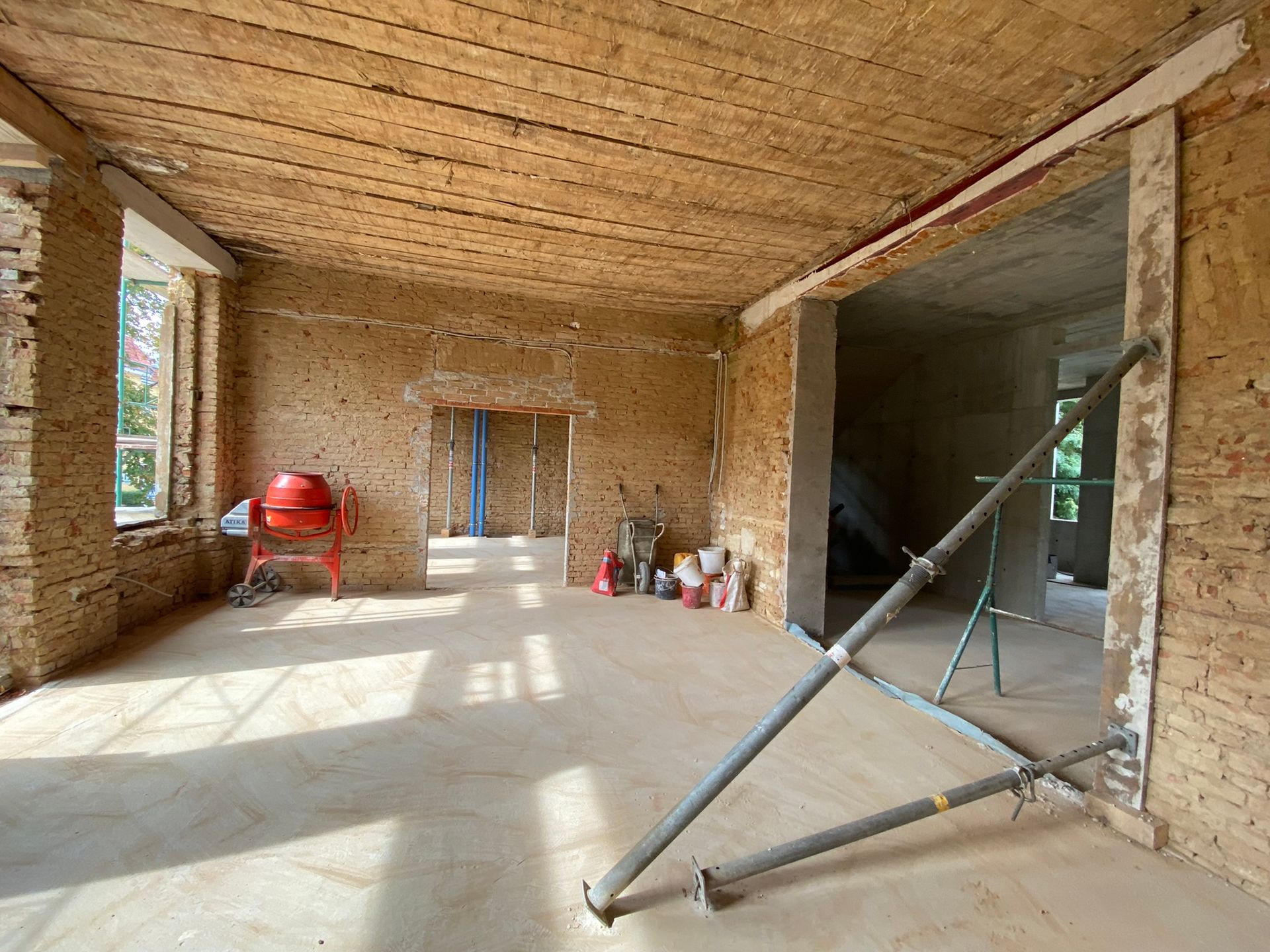 Innenbaustelle, Raum mit freiliegenden Erdwänden und Holzdecke. Gerüst, Betonmischer und Türen.