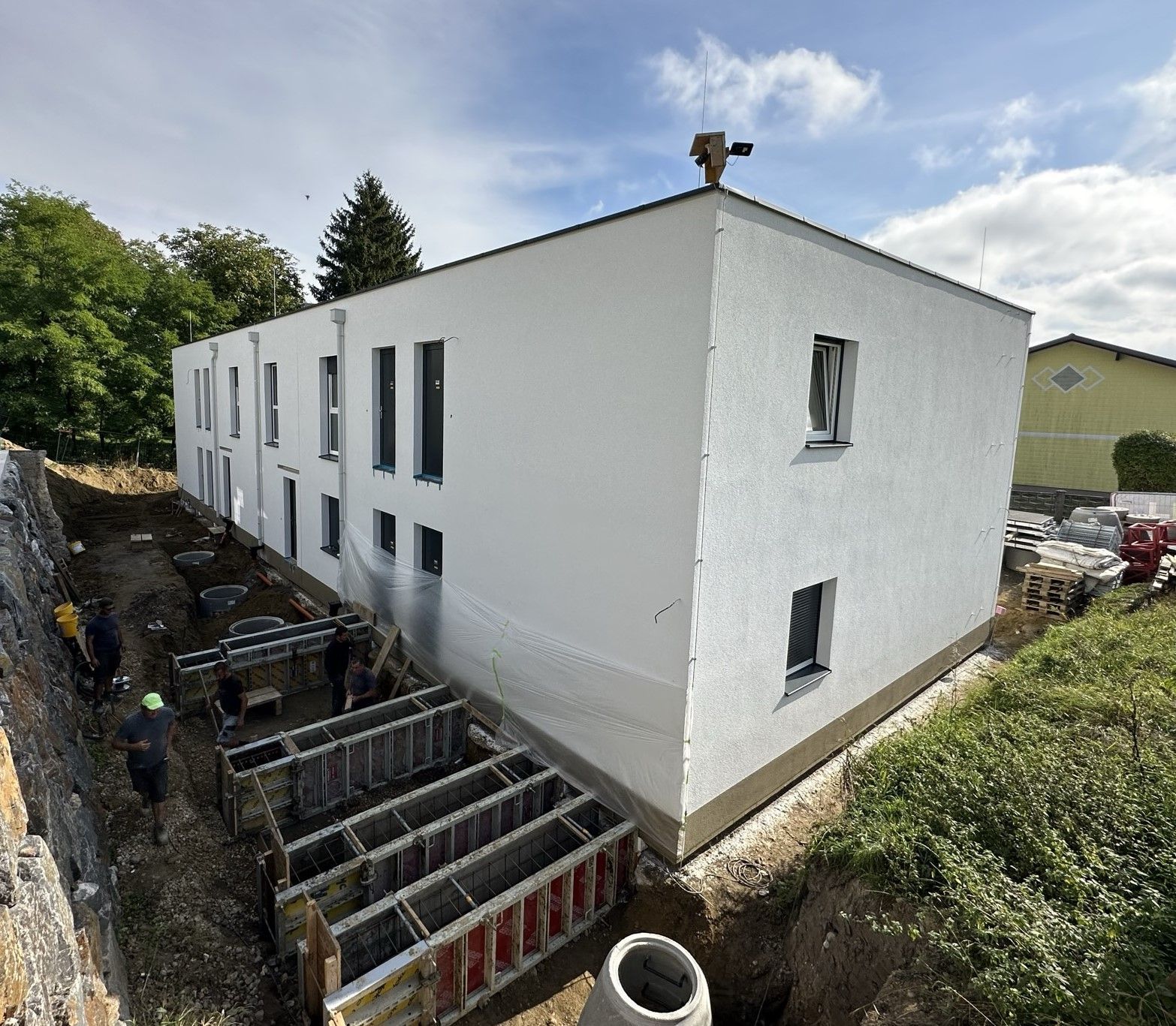 Baustelle mit einem weißen Gebäude, Arbeitern und Stützmauern.