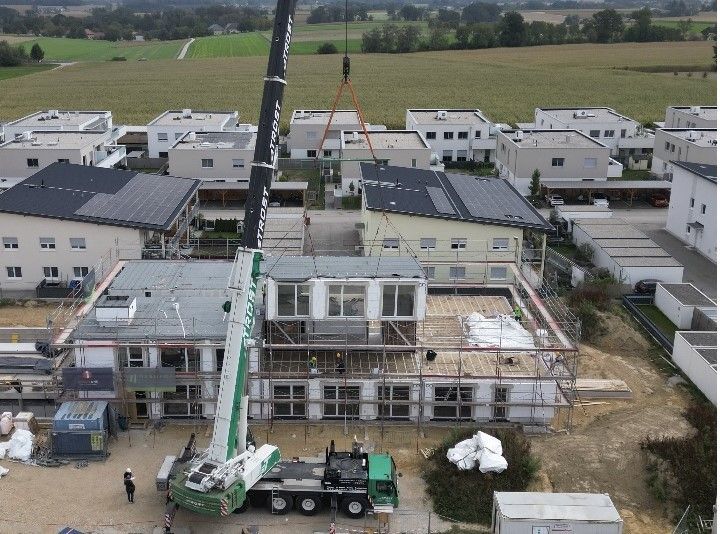 Ein Kran hebt eine modulare Baueinheit auf eine Baustelle in einem Wohngebiet.