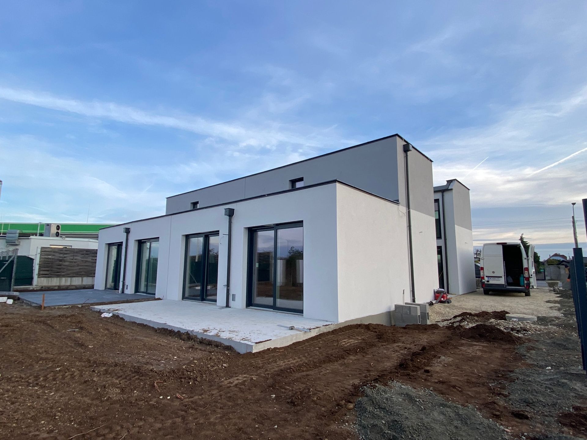 Modernes weißes Haus im Bau mit Flachdach und großen Fenstern. Bewölkter Himmel, Schmutz im Vordergrund.