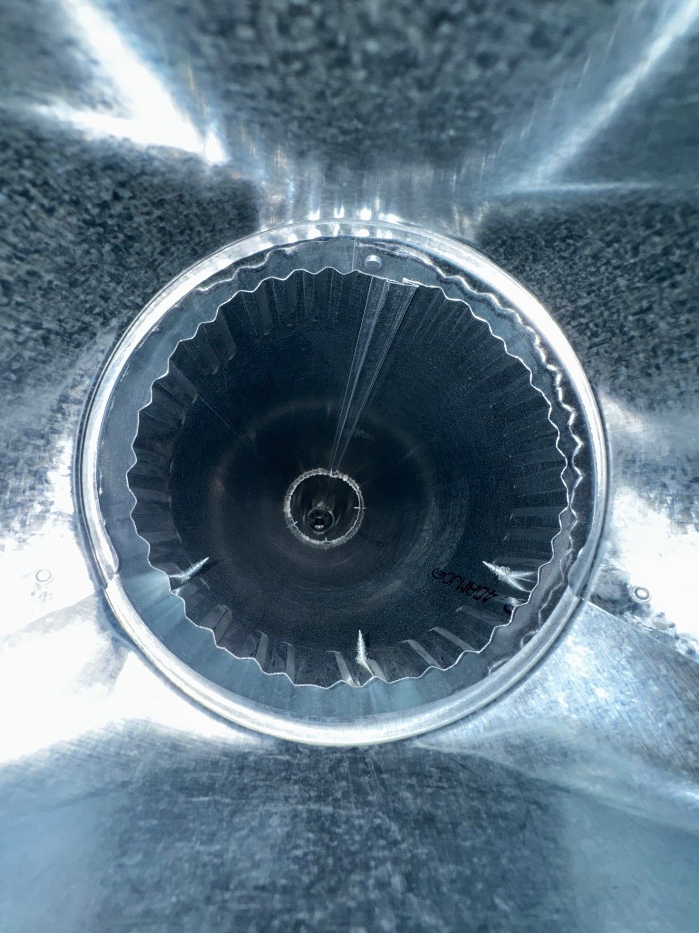 Inside view of a metallic tube. The circular opening has jagged edges with a smaller, central hole.