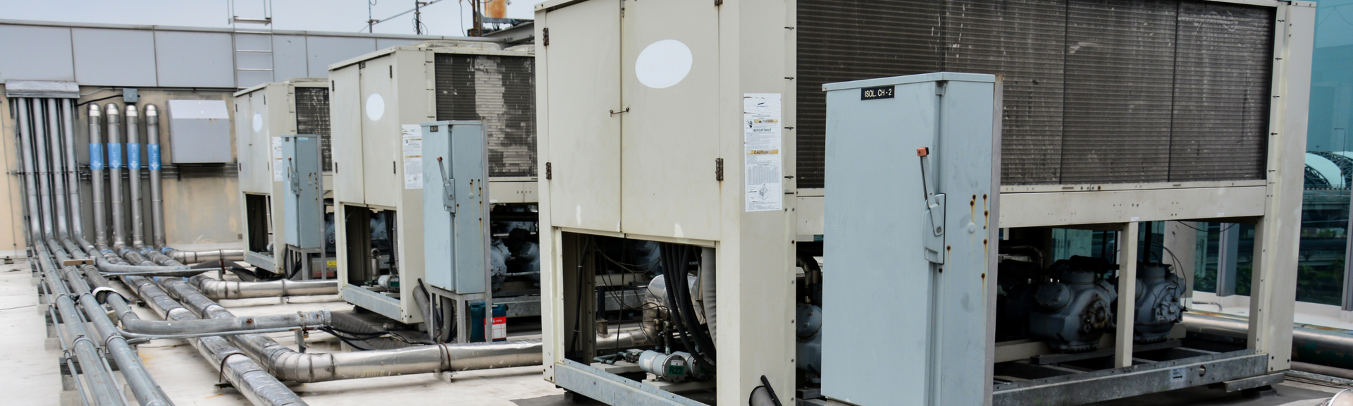 Four industrial HVAC chiller units lined up on a building rooftop next to metal electrical conduits.