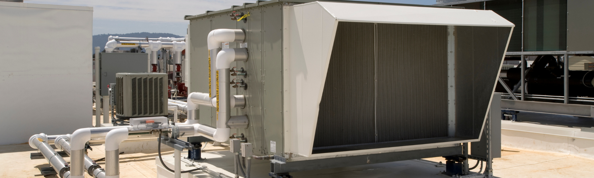Industrial HVAC equipment with external cooling coils and connected metal pipes installed on a rooftop.
