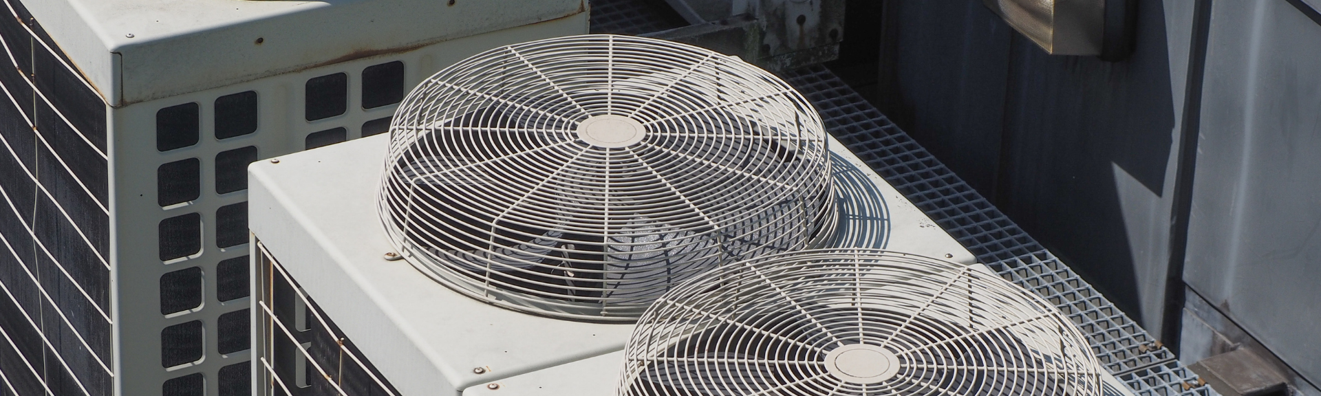 High-angle close-up of two large, industrial air conditioning unit fans with protective metal grates on a rooftop.