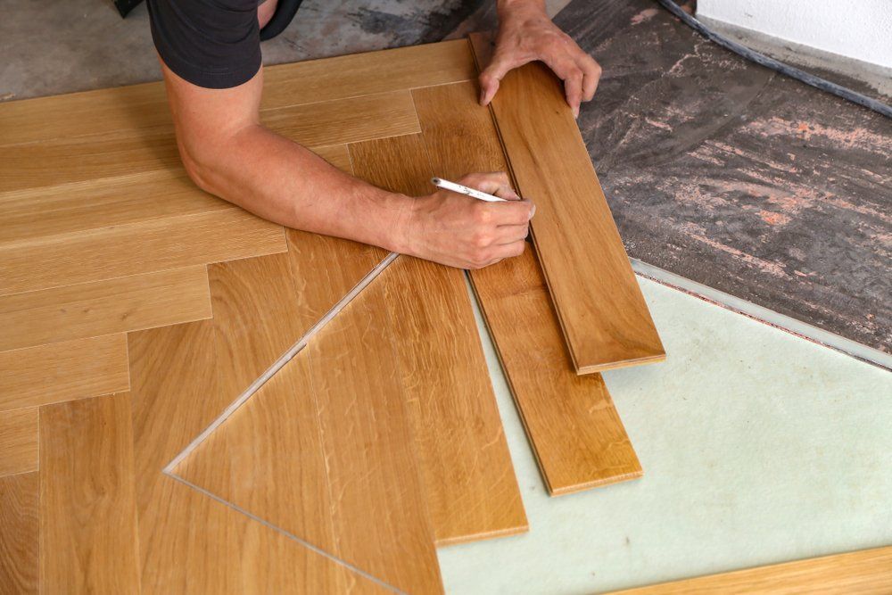 Une personne trace et coupe des lames de parquet à l'aide d'un crayon et d'une règle sur une surface de travail.