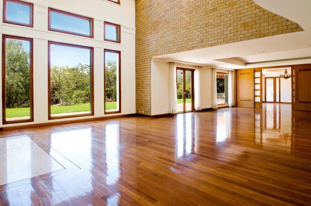 Salon lumineux et vide avec parquet ciré, hautes fenêtres et mur de cheminée en briques