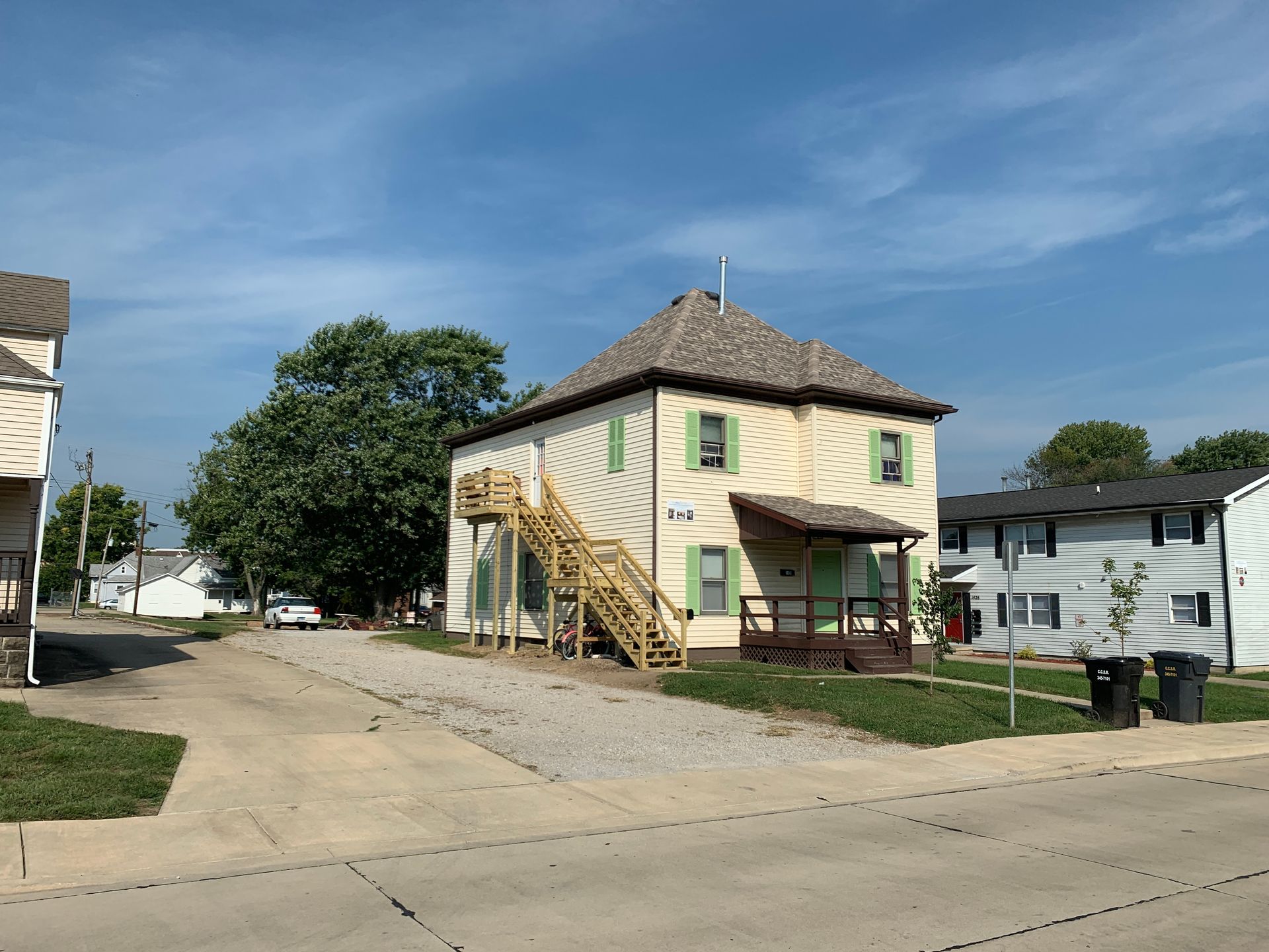 A house with stairs leading up to the second floor is sitting on the corner of a street.