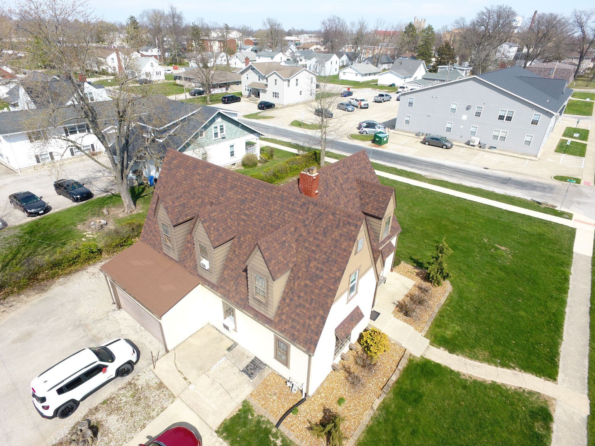 An aerial view of a house in a residential area with cars parked in front of it.