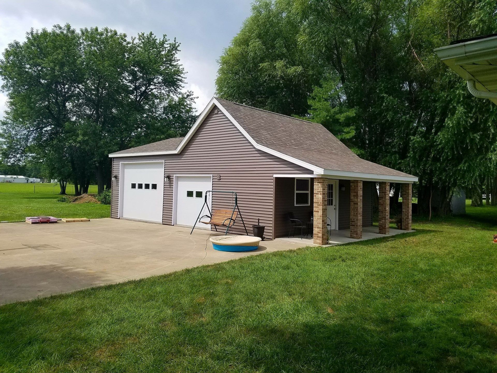 A garage with a porch and a pool in front of it.