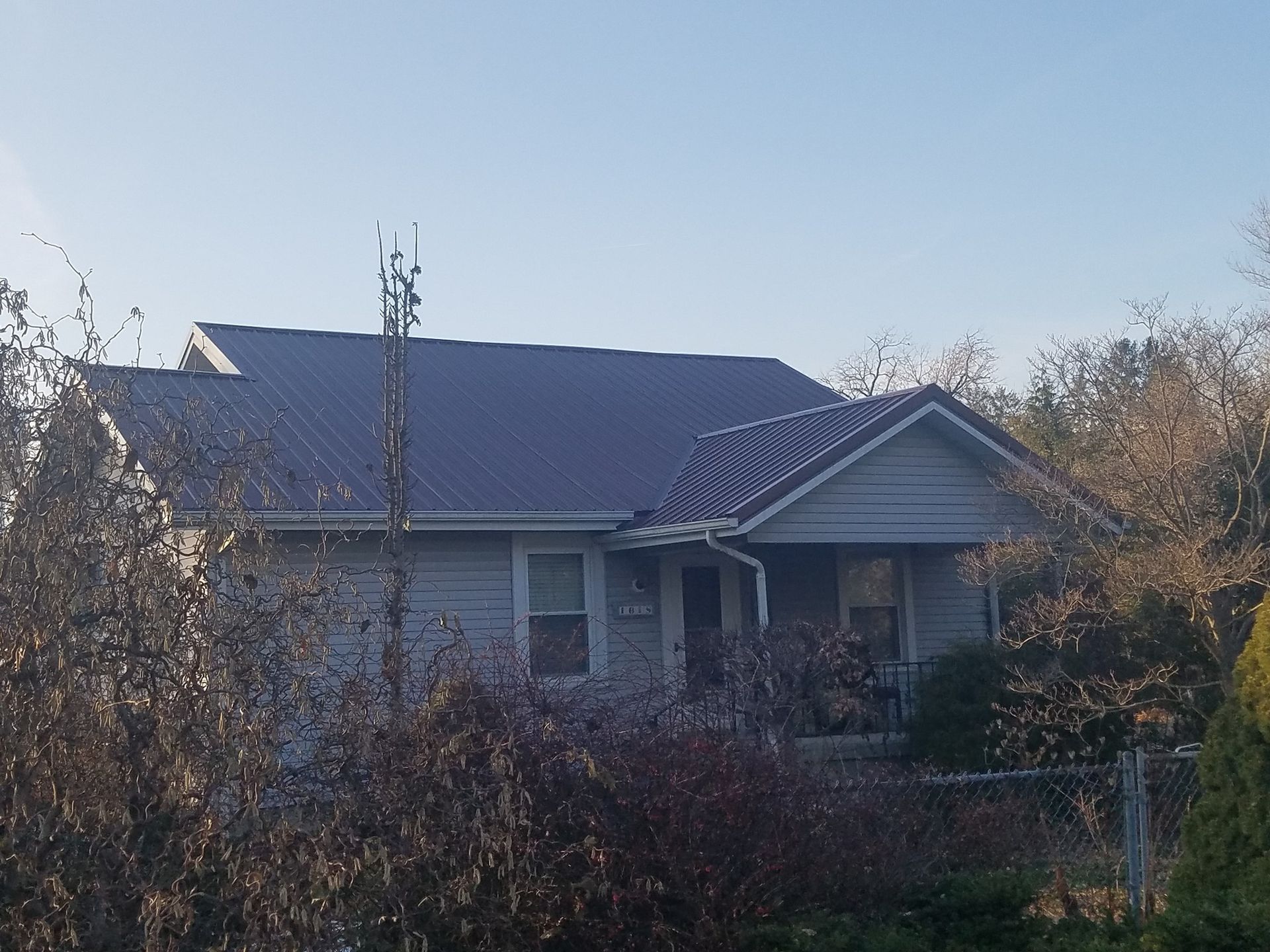 A white house with a blue roof is surrounded by trees and bushes.