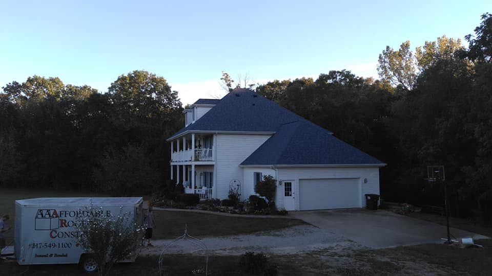 A large white house with a blue roof is surrounded by trees