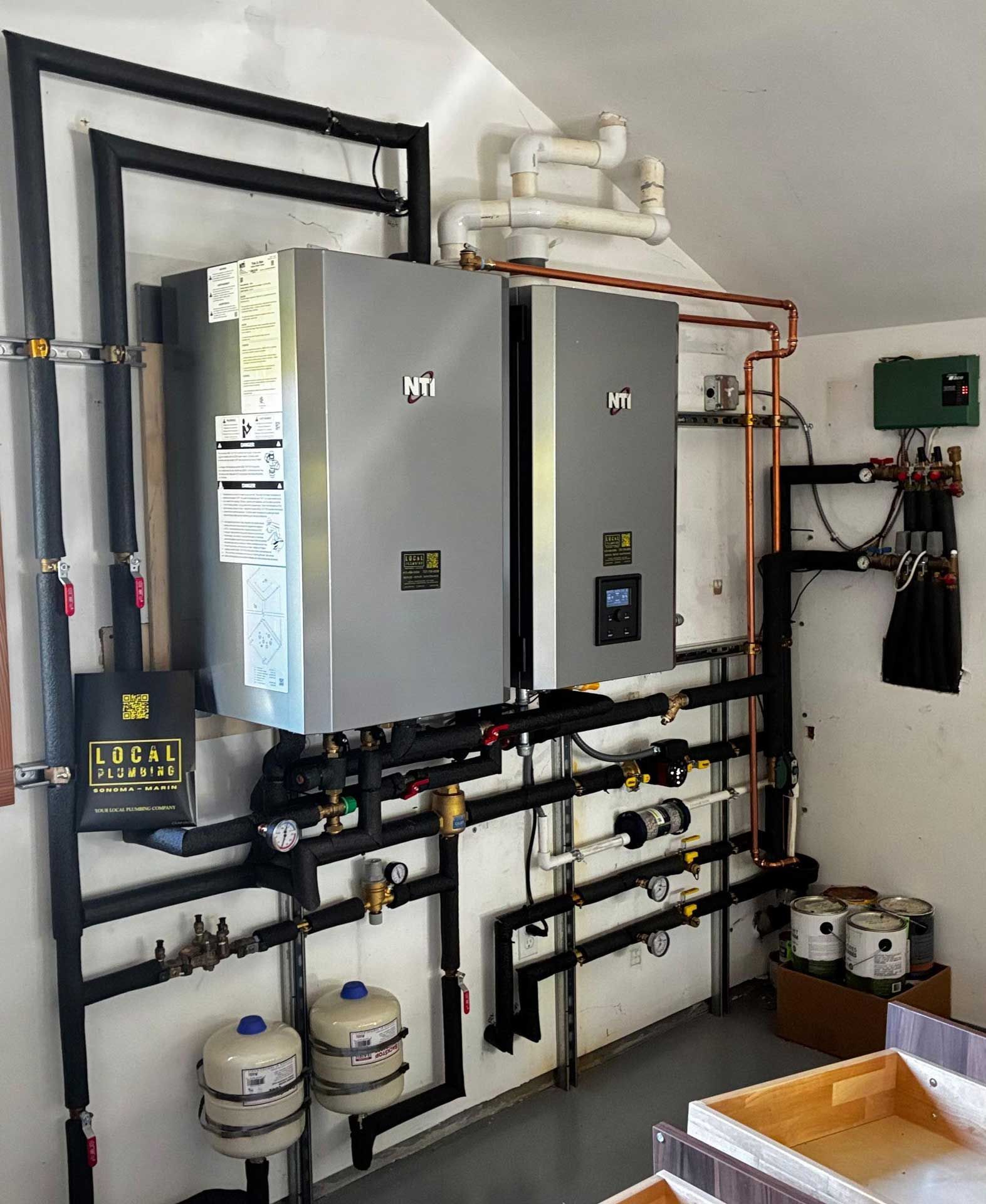 Two gray heating units installed on a wall with various connected pipes and components.