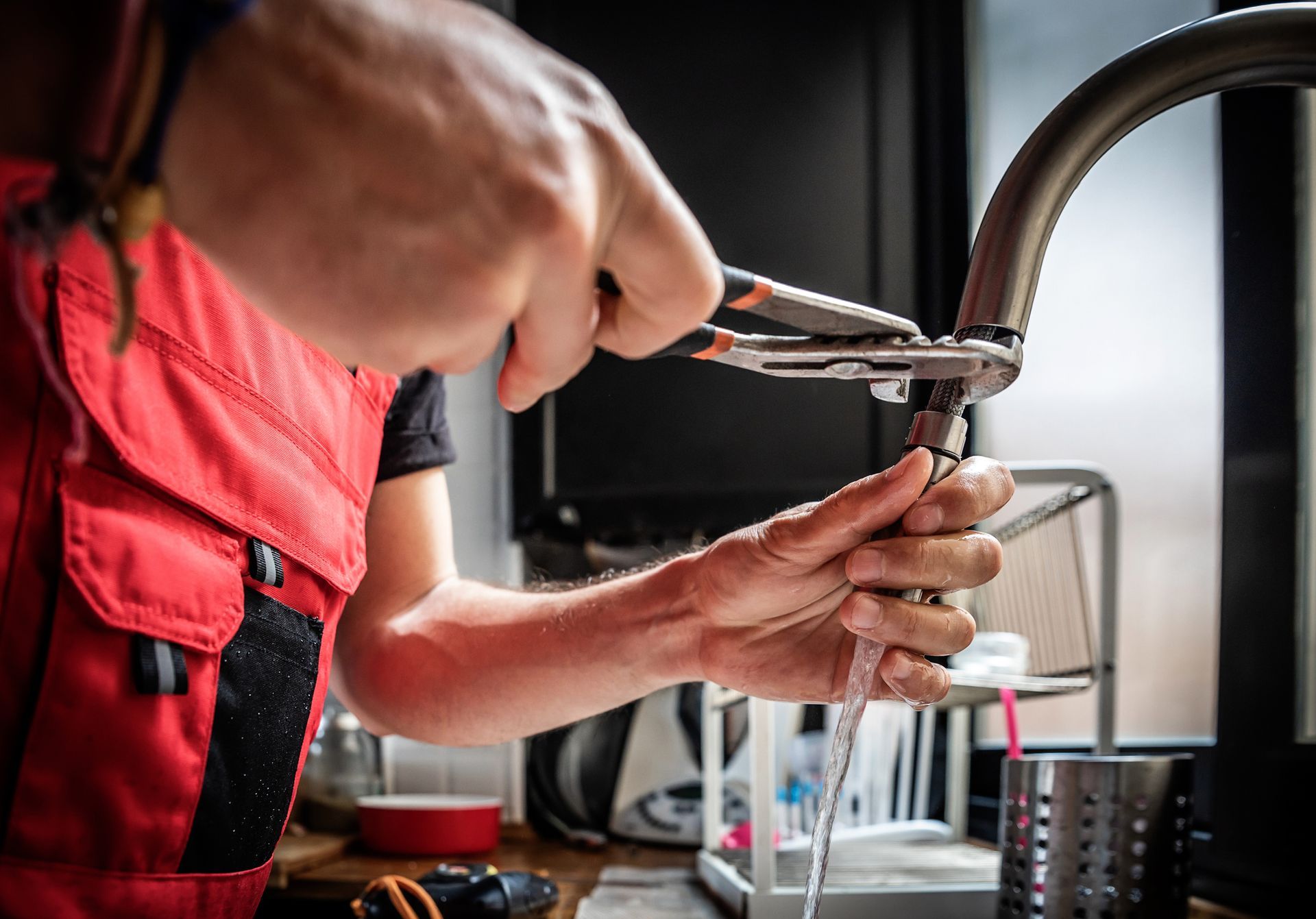 A man wearing a red apron is fixing a faucet, demonstrating professional plumbing services.
