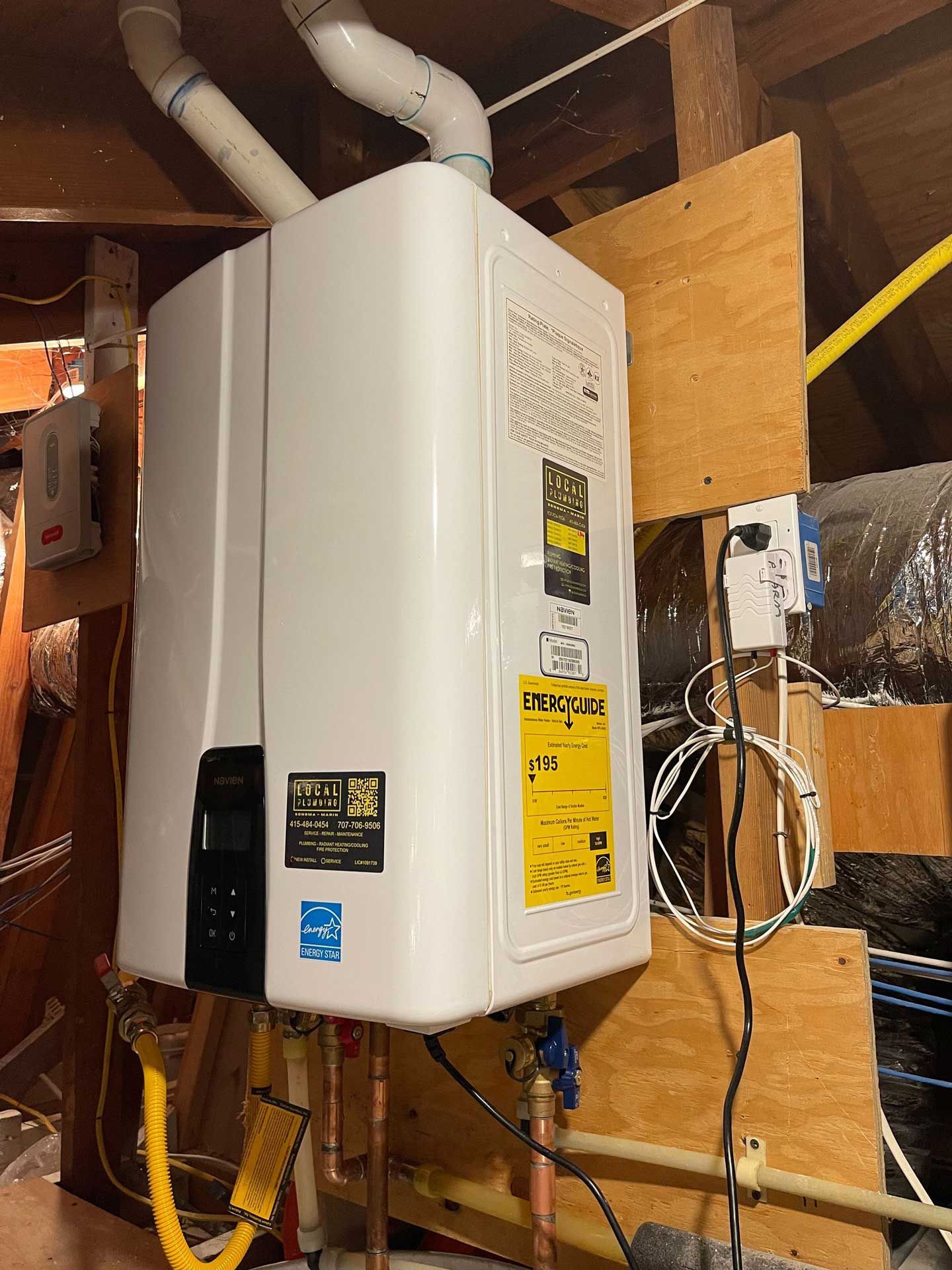 White tankless water heater mounted on a wooden wall, pipes and vents visible.