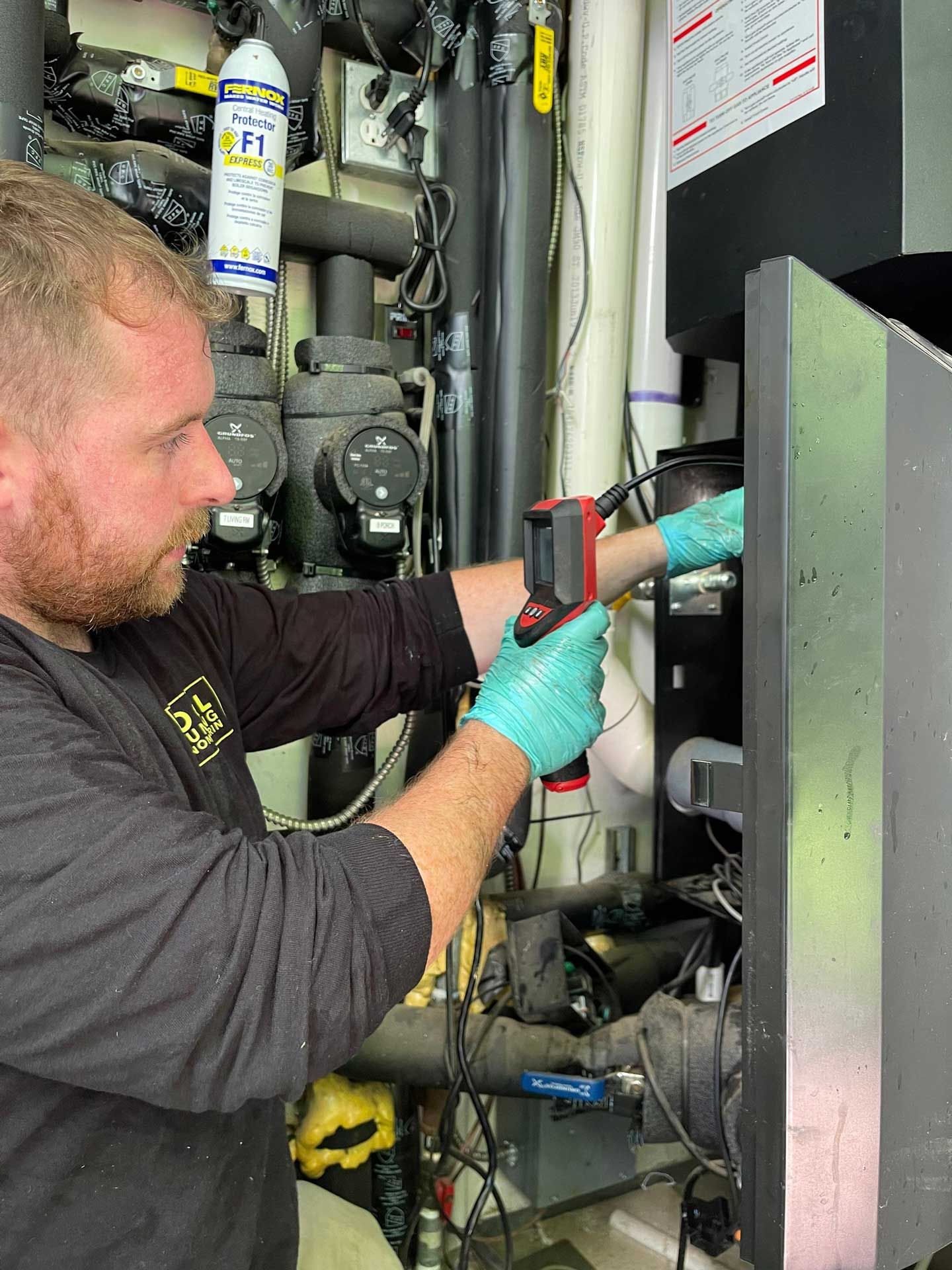 Man in gloves uses a temperature gun on machinery in an equipment room.