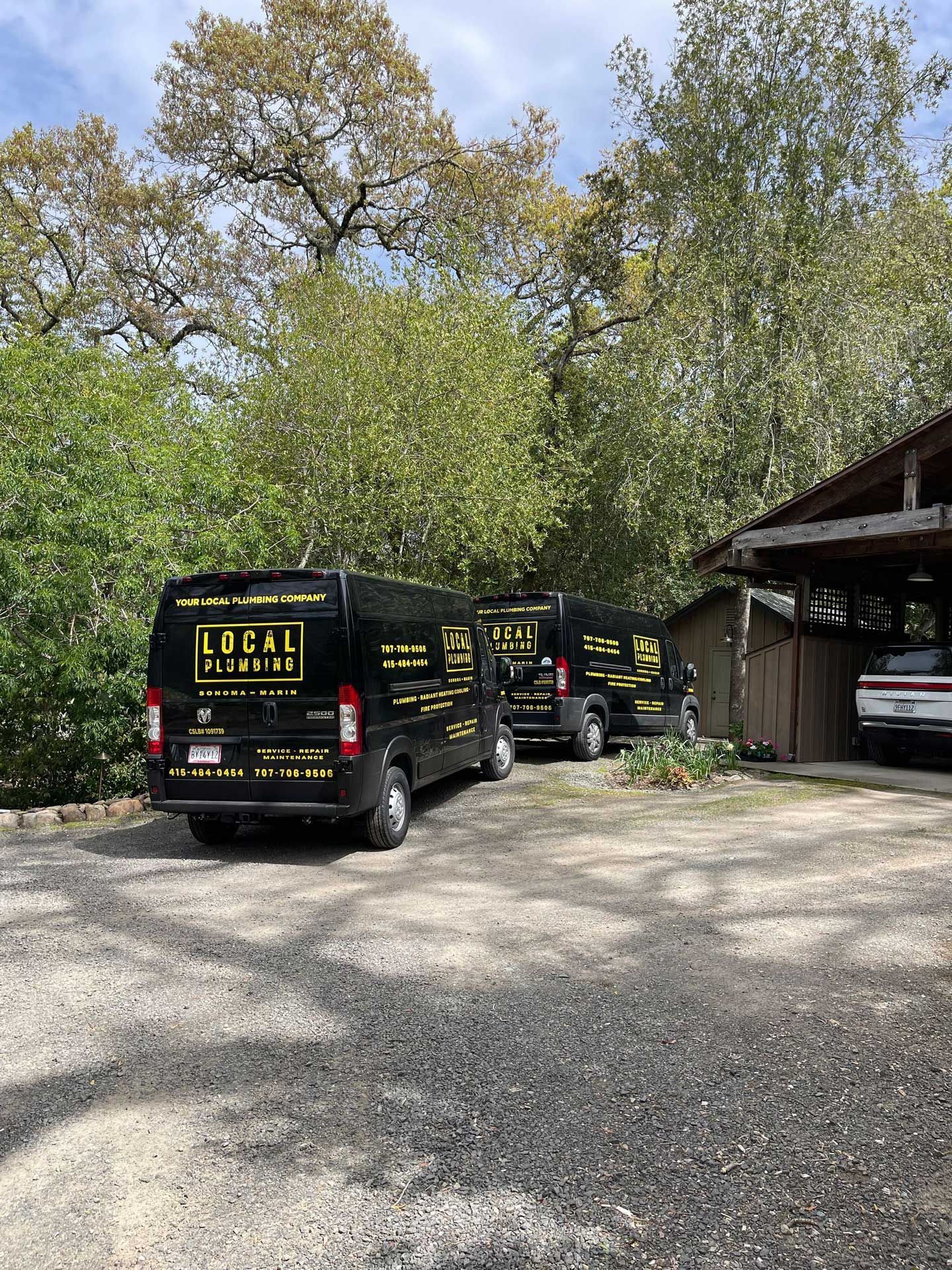 Three black vans with yellow text parked in a gravel lot near a wooden structure and trees.