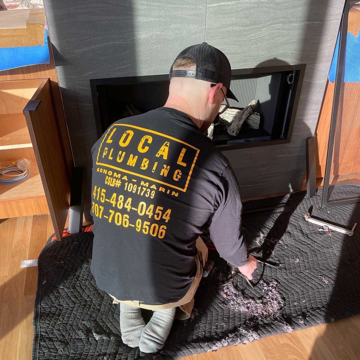 Plumber working on a fireplace. Wearing black shirt with 