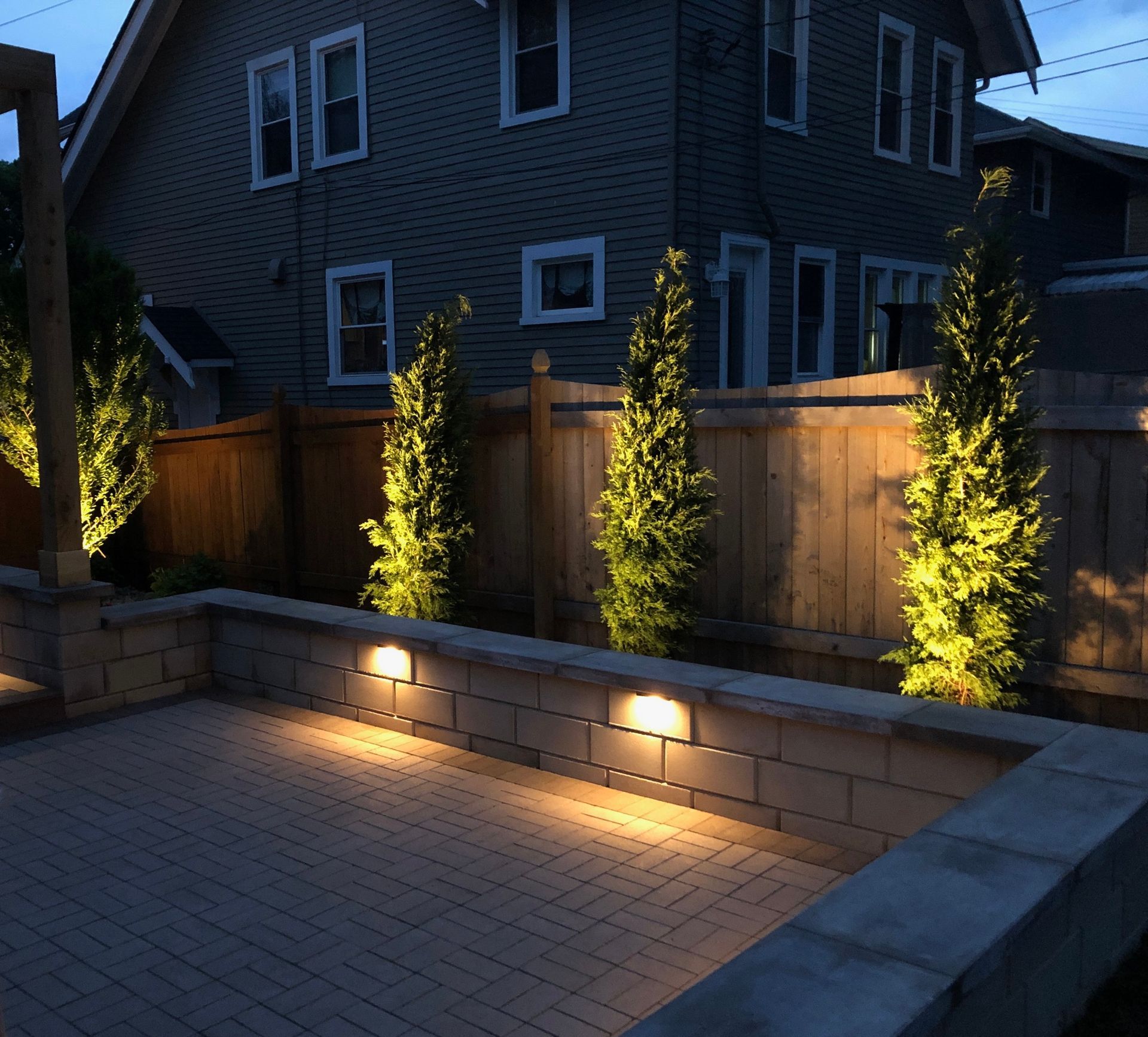 A house with a wooden fence and trees lit up at night