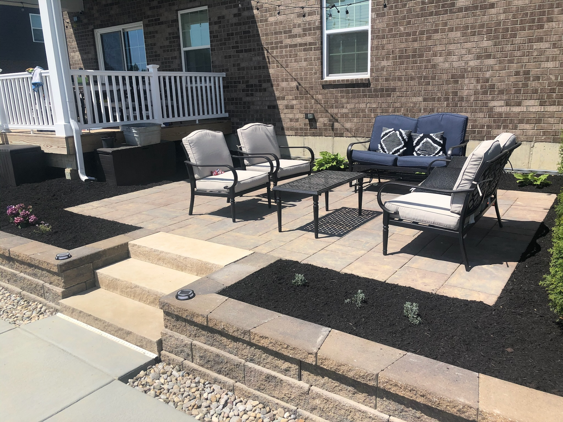 A patio with a couch , chairs , and a table in front of a brick house.