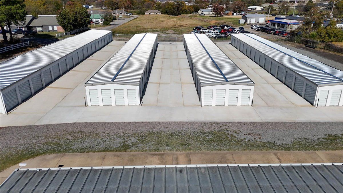 Aerial view of four rows of white storage units with wavy gray roofs on a concrete lot.