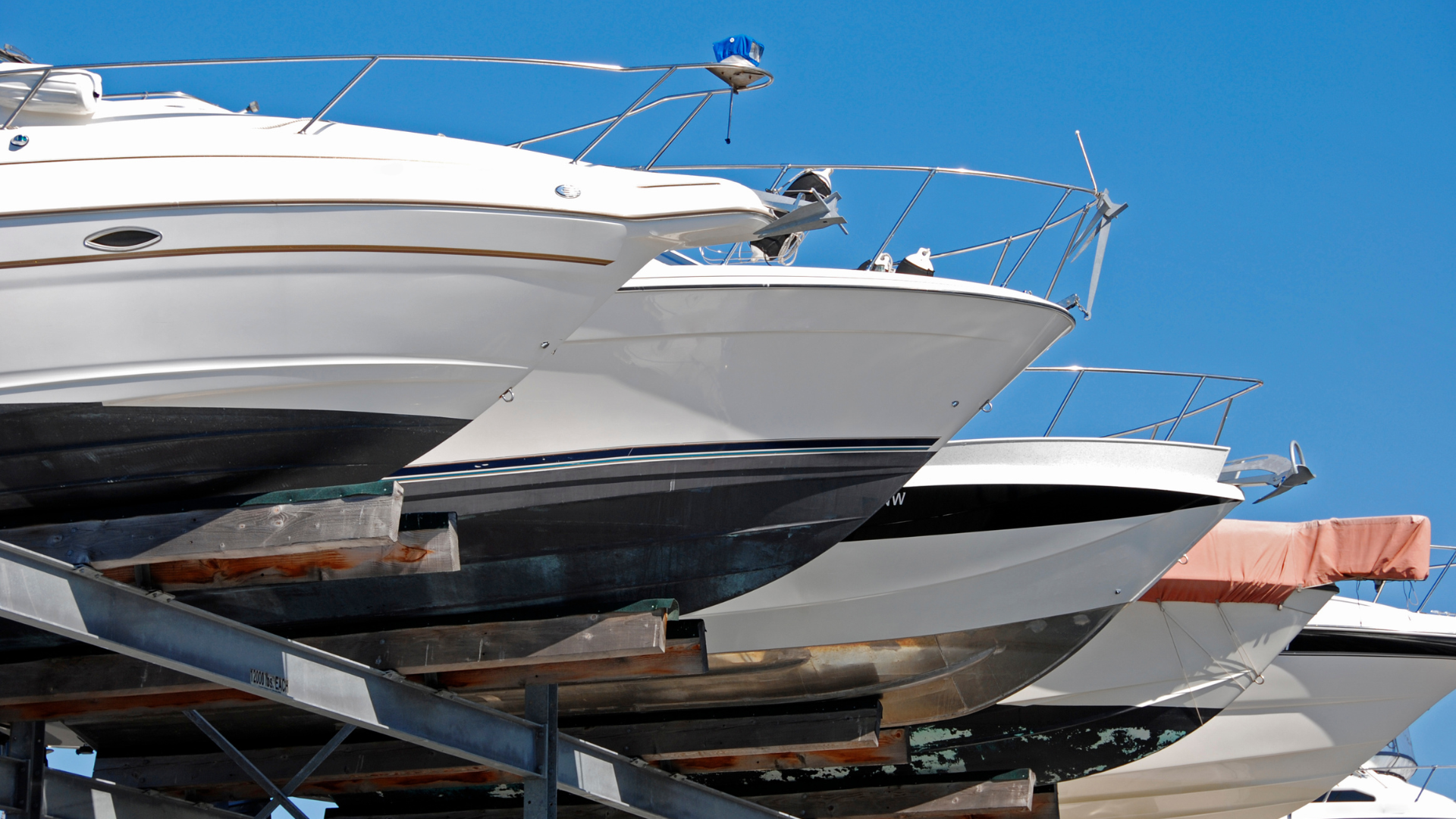 Boats stacked on metal racks, white hulls against a clear blue sky.
