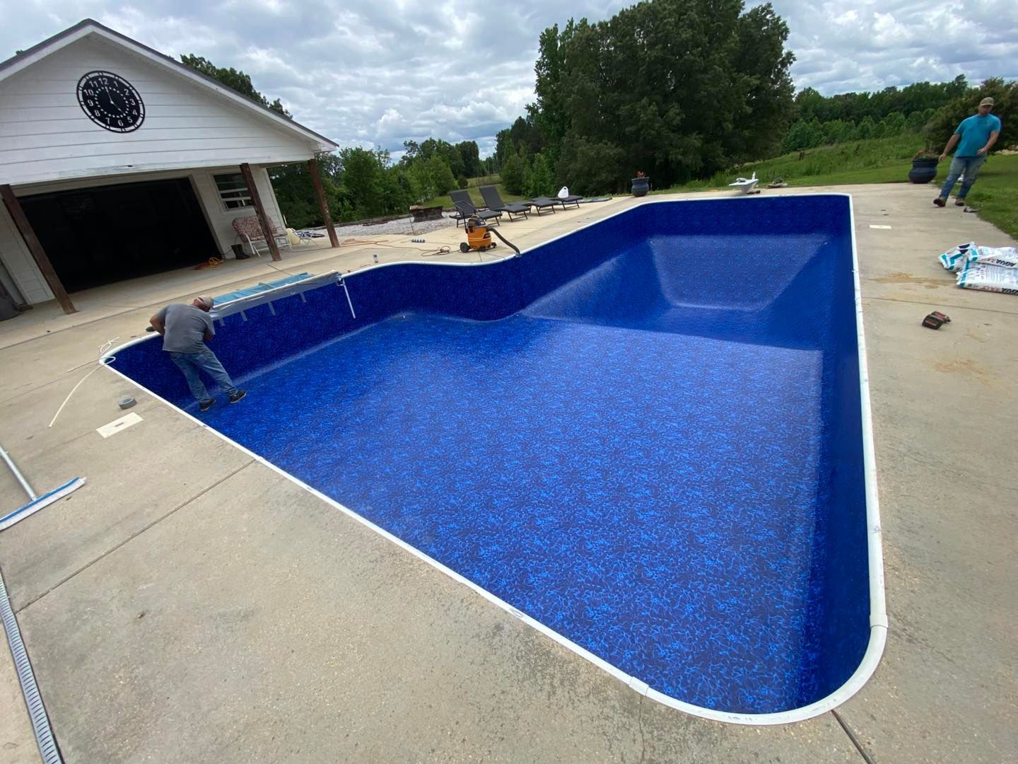 A worker installing a deep blue vinyl liner in a large, empty residential inground swimming pool.