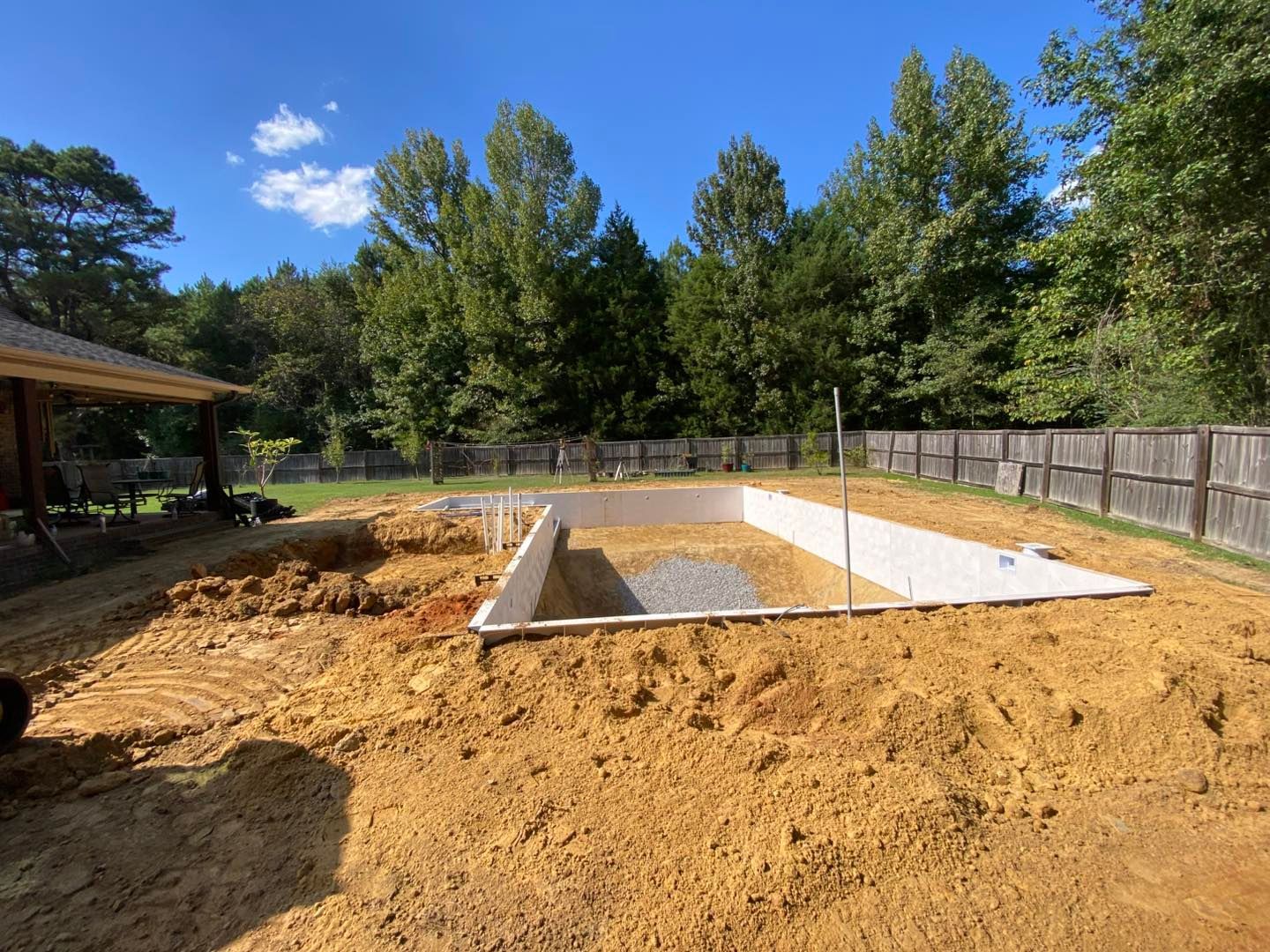 An rectangular in-ground swimming pool under construction, showing white panel walls, gravel base, and dirt excavation.