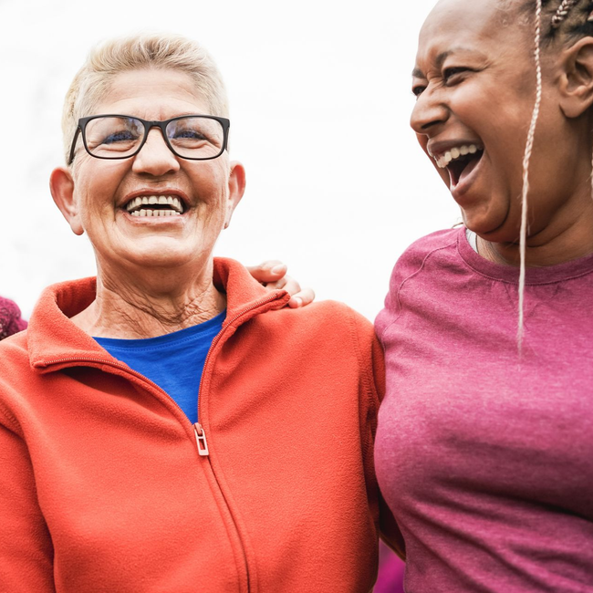 Two people laughing together, one wearing an orange fleece jacket and glasses, the other in a magenta top.
