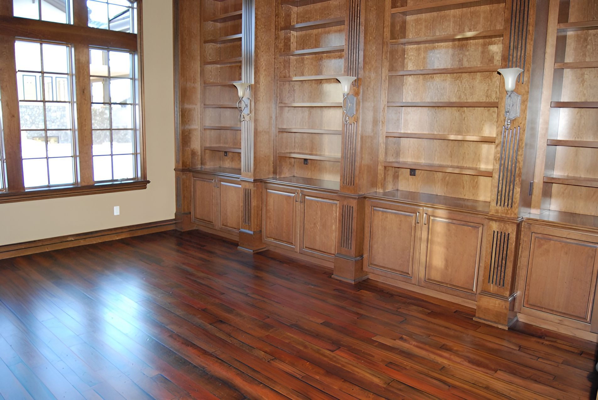 Wooden bookshelves and cabinets with hardwood floor next to a window.