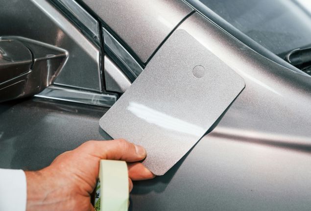 A person is holding a sponge in front of a car.