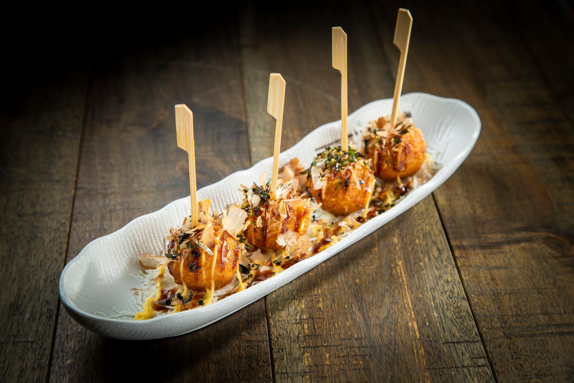 Appetizer skewers with sesame seeds and sauce served on a white platter on a rustic wooden table