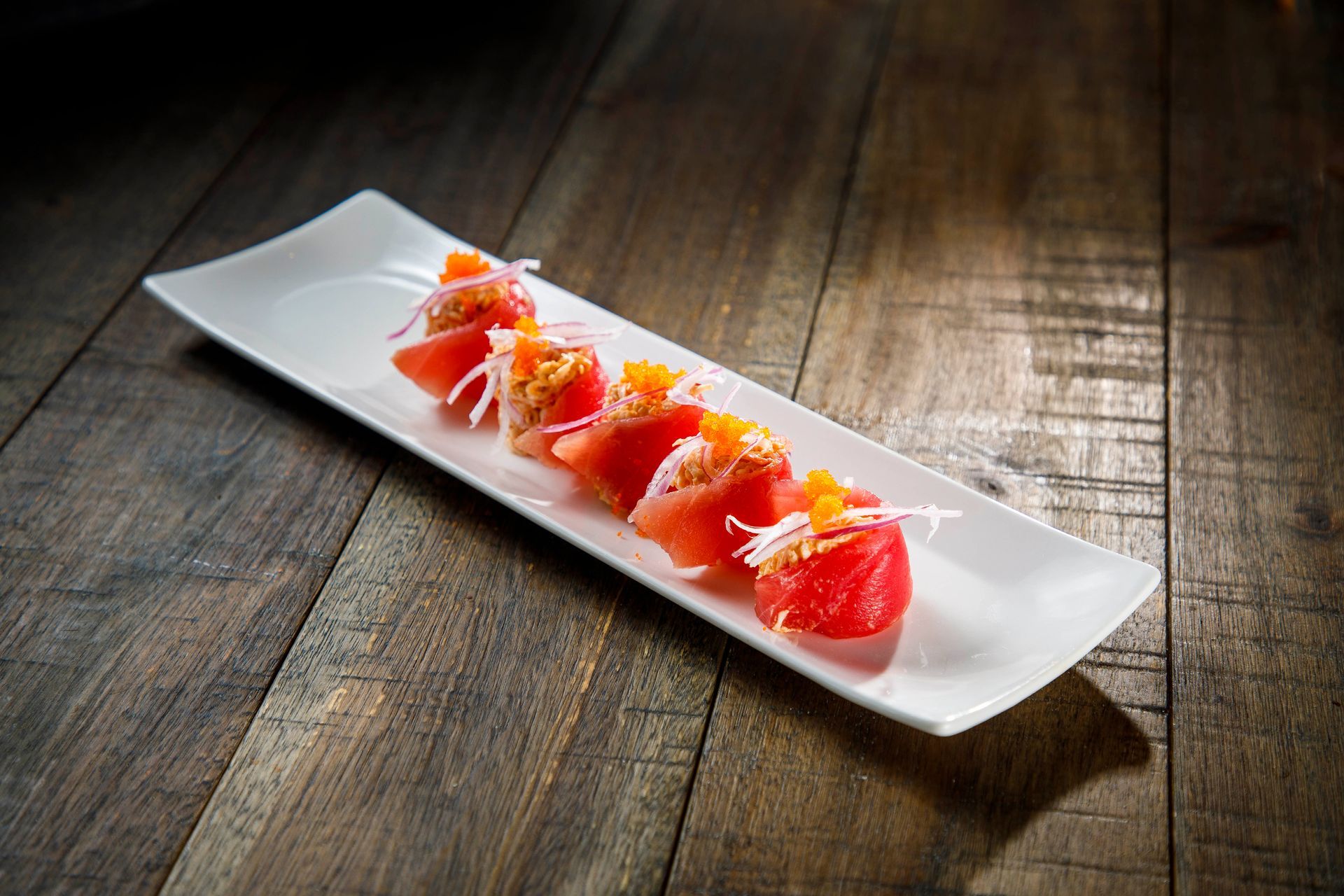 White rectangular plate with sliced strawberries and cream on a rustic wooden table