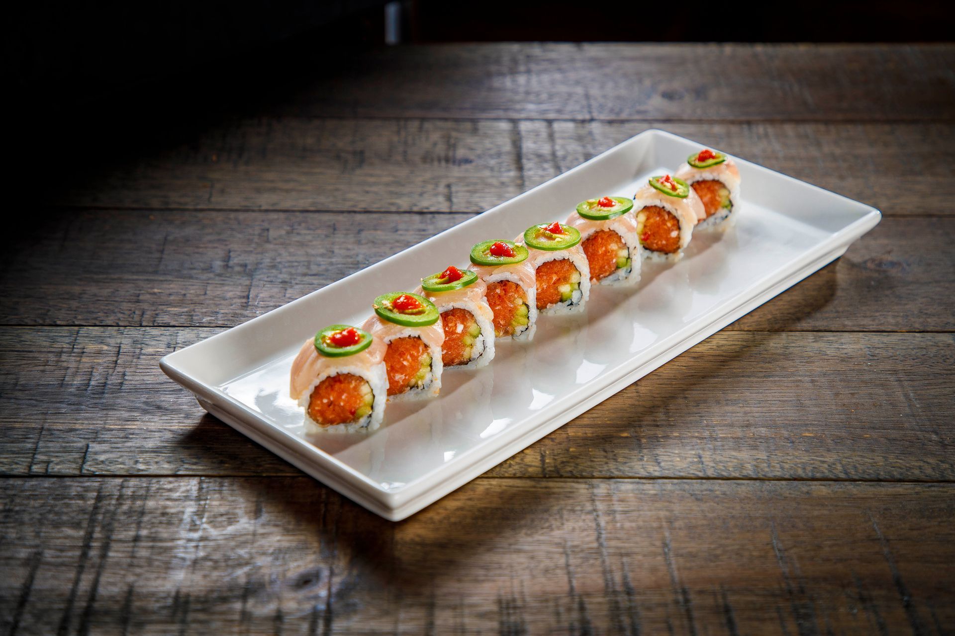 Sushi rolls topped with salmon and roe arranged on a long white platter on a rustic wooden table