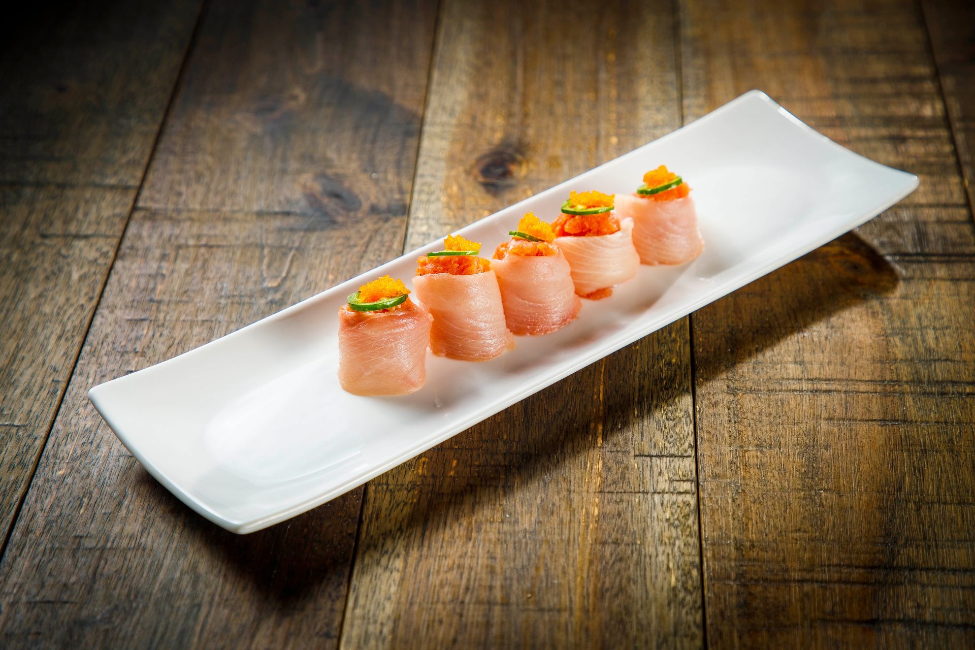 Sushi rolls topped with orange garnish on a long white platter on a wooden table