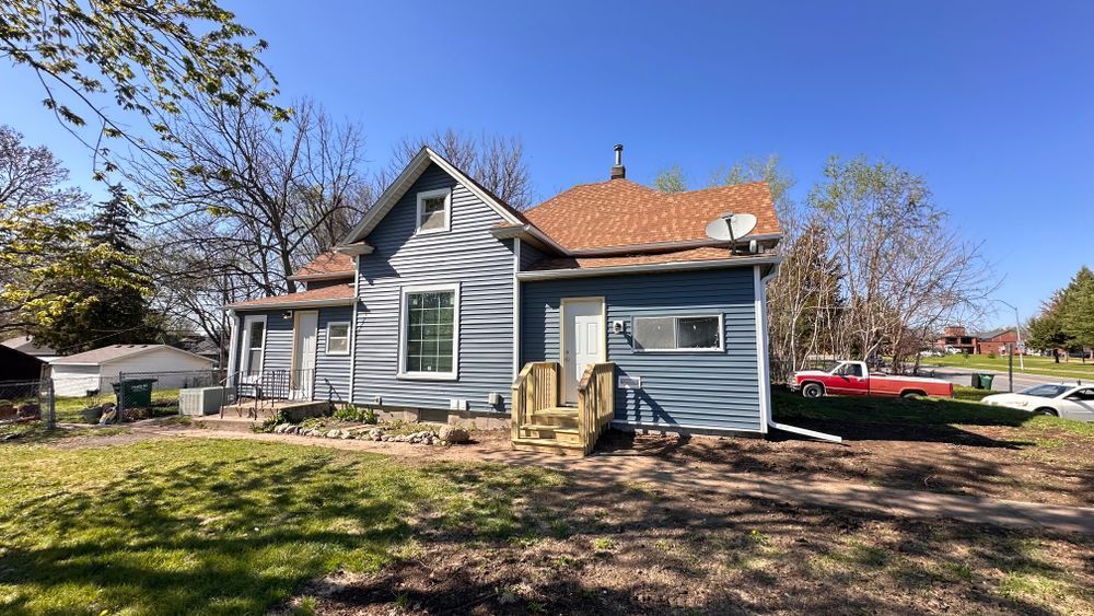 Blue house with white trim, a red roof, and green yard under a blue sky.
