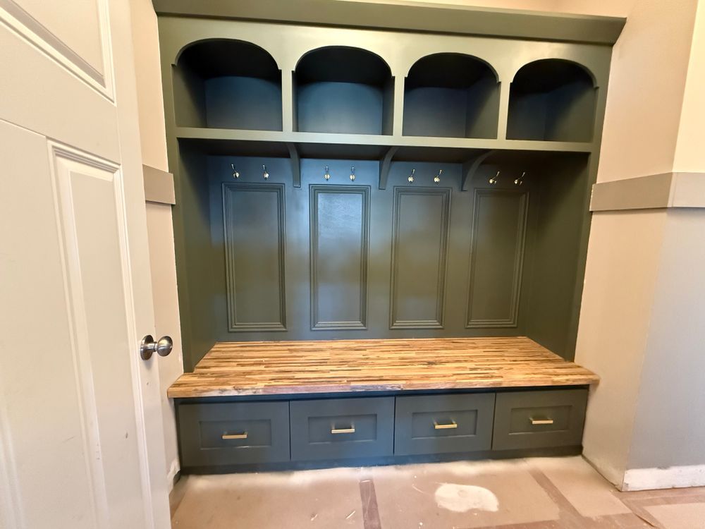 Green built-in entryway storage with arched shelving, hooks, bench, and drawers with gold hardware.