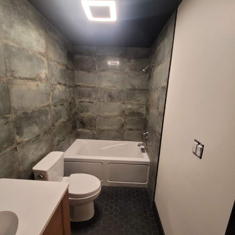 Bathroom with dark gray tile walls, white tub, and dark gray hexagon floor.