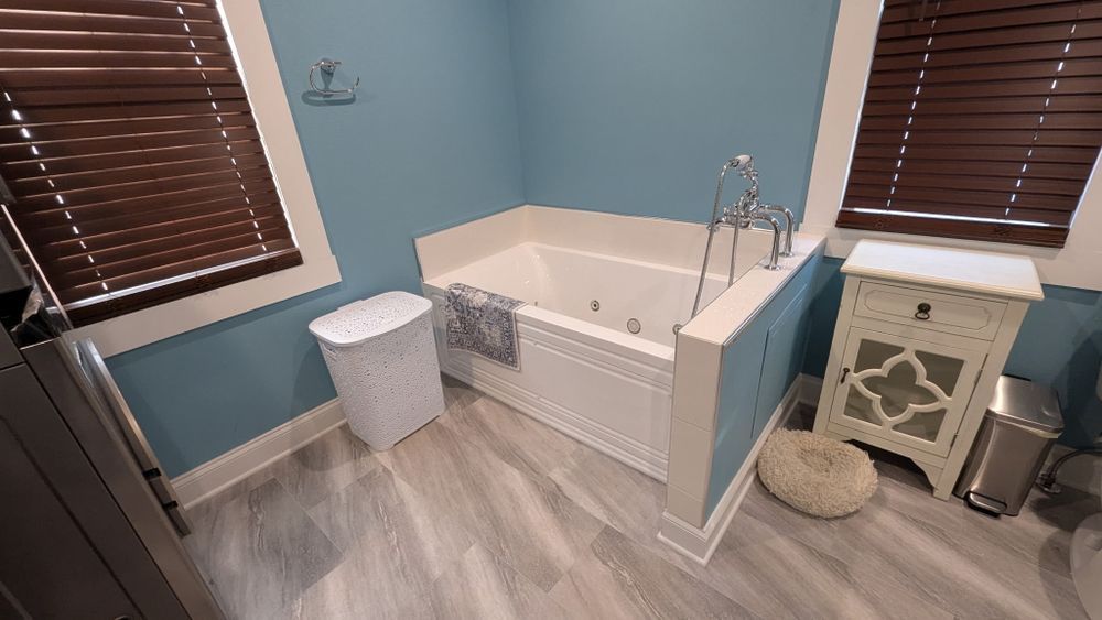 Bathroom with a tub, blue walls, wood blinds, and wood-look floor.