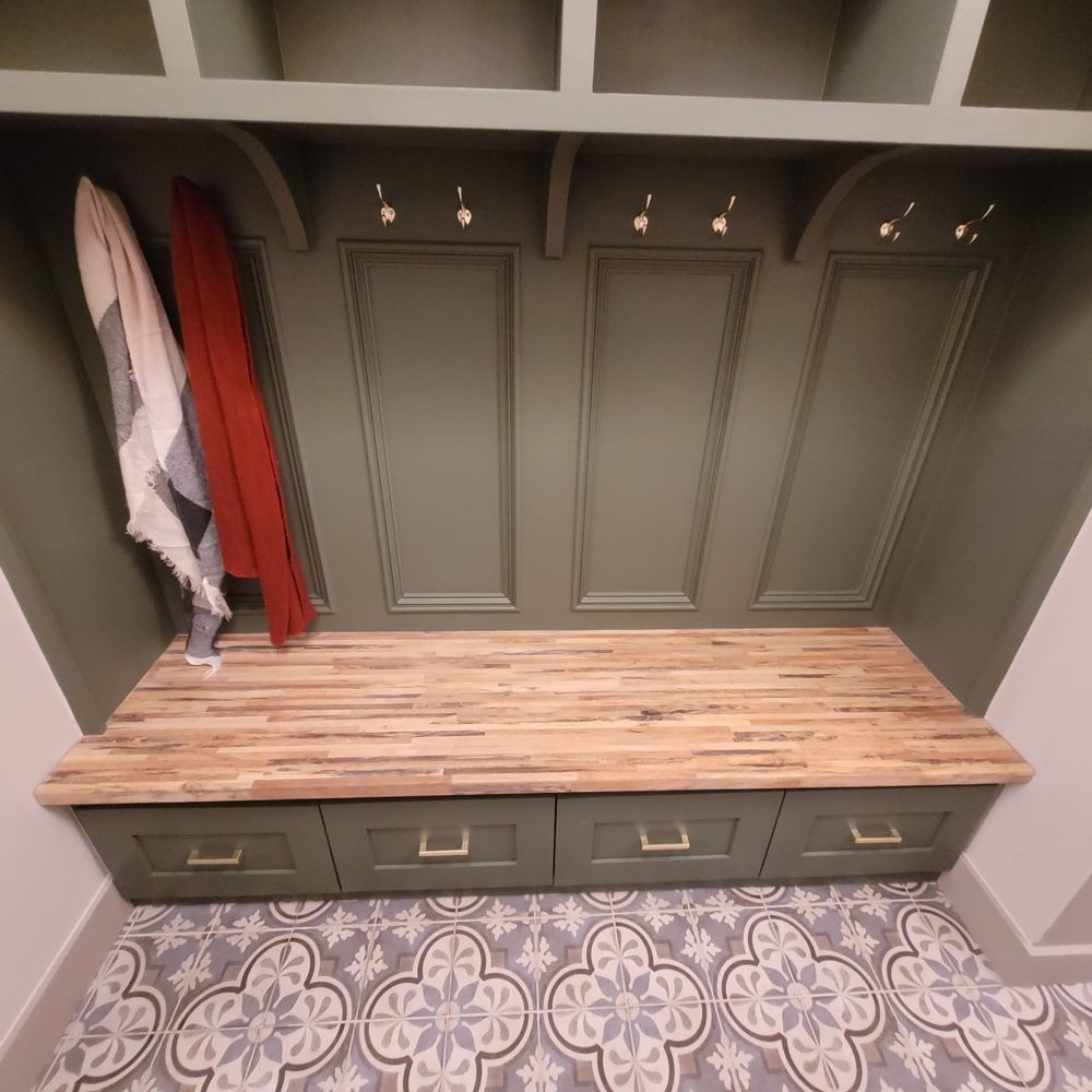 Green mudroom with wooden bench, storage, and hooks, with a patterned floor.